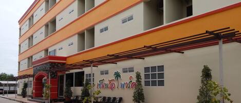 A multi-story building with a red and yellow facade, outdoor seating area, and potted plants.