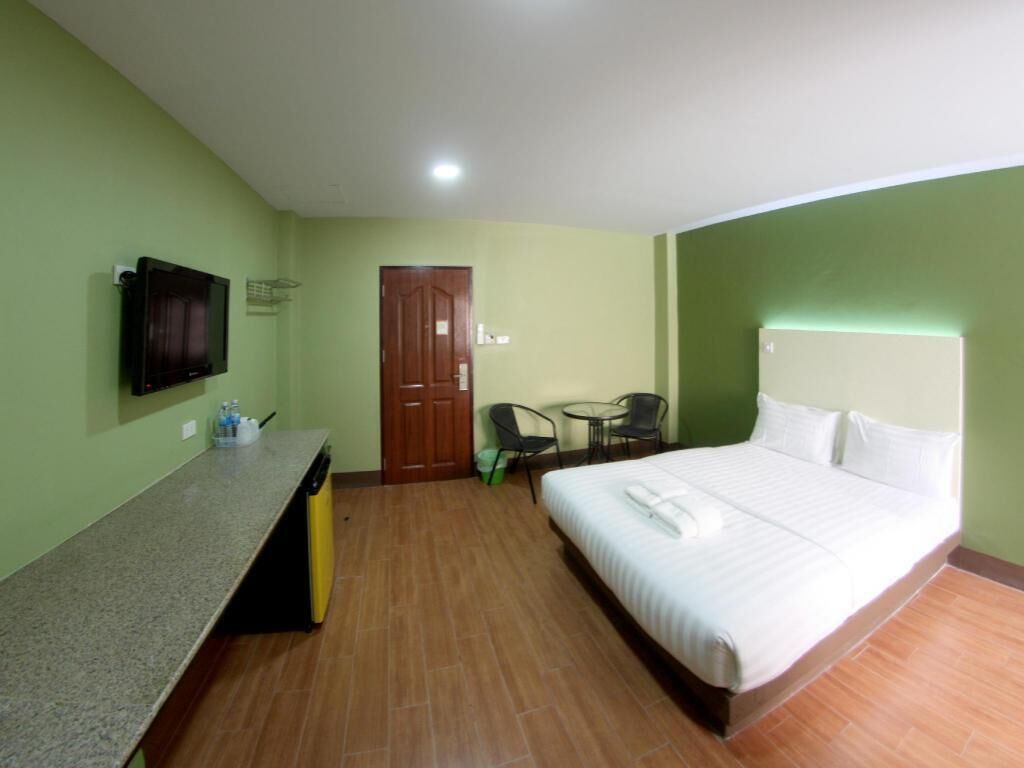 A hotel room with a bed, a TV mounted on the wall, a small table with chairs, and a door.