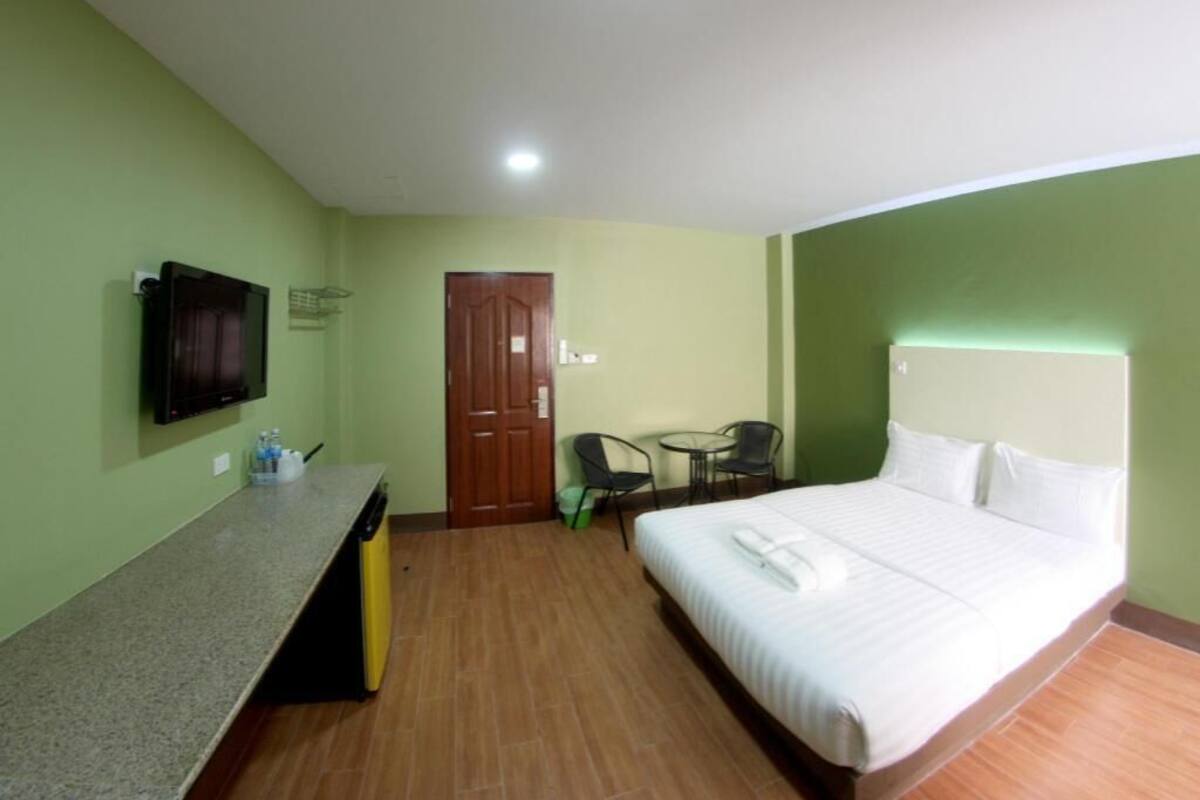 A hotel room with a bed, a TV mounted on the wall, a small table with chairs, and a door.