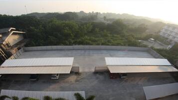 Un amplio estacionamiento al aire libre con dos zonas techadas, rodeado de vegetación y edificios.