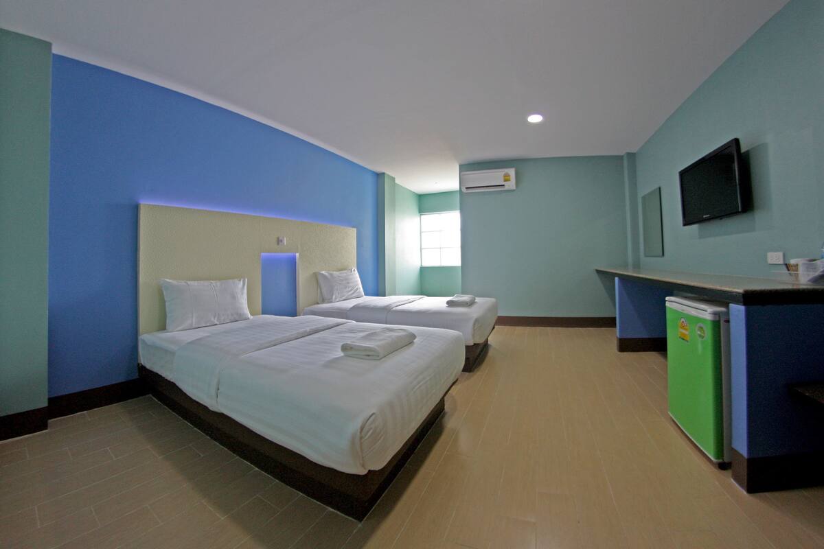 A hotel room with two beds, a desk, a television, and an air conditioning unit.