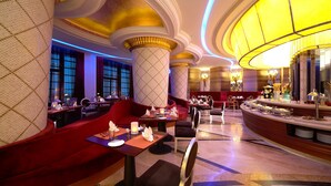 Un lobby de hotel lujoso con asientos rojos, una zona de buffet y columnas ornamentales.