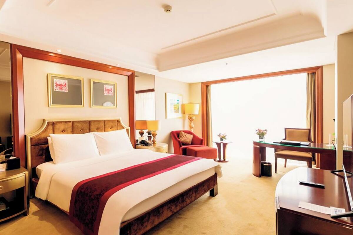 Ein Hotelzimmer mit einem großen Bett, Nachttischen, einem Schreibtisch, einem Sessel, einem Fernseher und gerahmten Bildern an der Wand.
