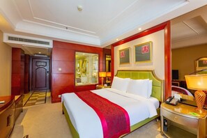 Une chambre d’hôtel avec un grand lit, une table de chevet avec une lampe, un miroir et une porte donnant sur une autre pièce.