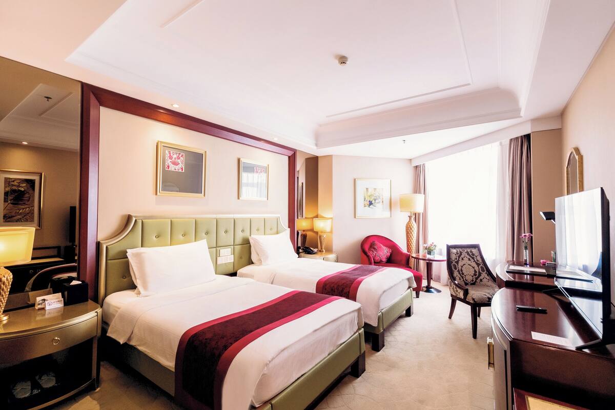 Ein Hotelzimmer mit zwei Betten, einem Schreibtisch, einem Sessel, einem Fernseher und Bildern an den Wänden.