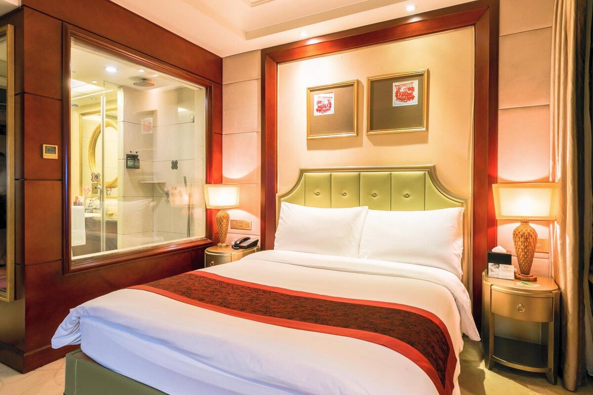 Ein Hotelzimmer mit einem großen Bett, einem Spiegel, zwei gerahmten Bildern an der Wand und einem Nachttisch mit einer Lampe.