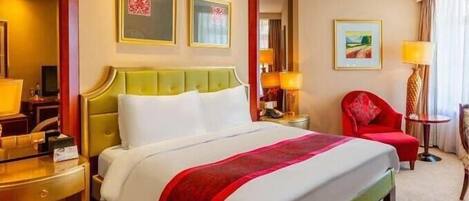 A hotel room with a large bed, a desk, a chair, and two paintings on the wall.