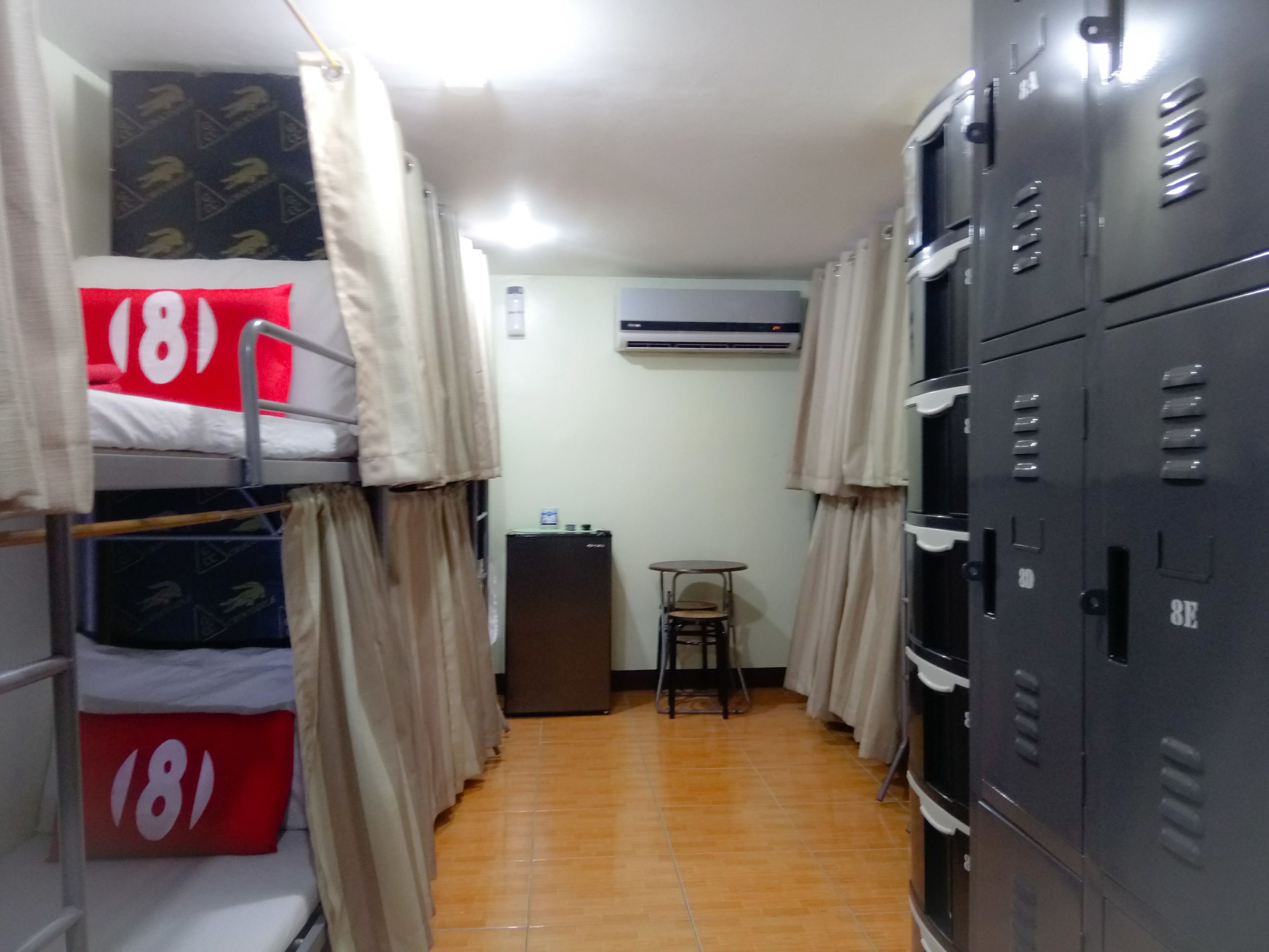 A narrow corridor with bunk beds labeled '18' and '19', a small table, and a refrigerator.