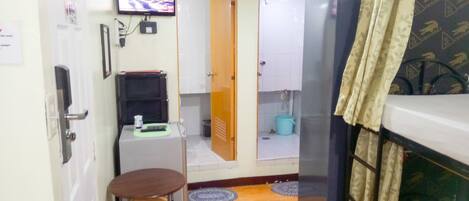 Una cuina compacta amb nevera, una taula petita amb tamborets, una televisió penjada a la paret i un bany visible a través d'una porta oberta.