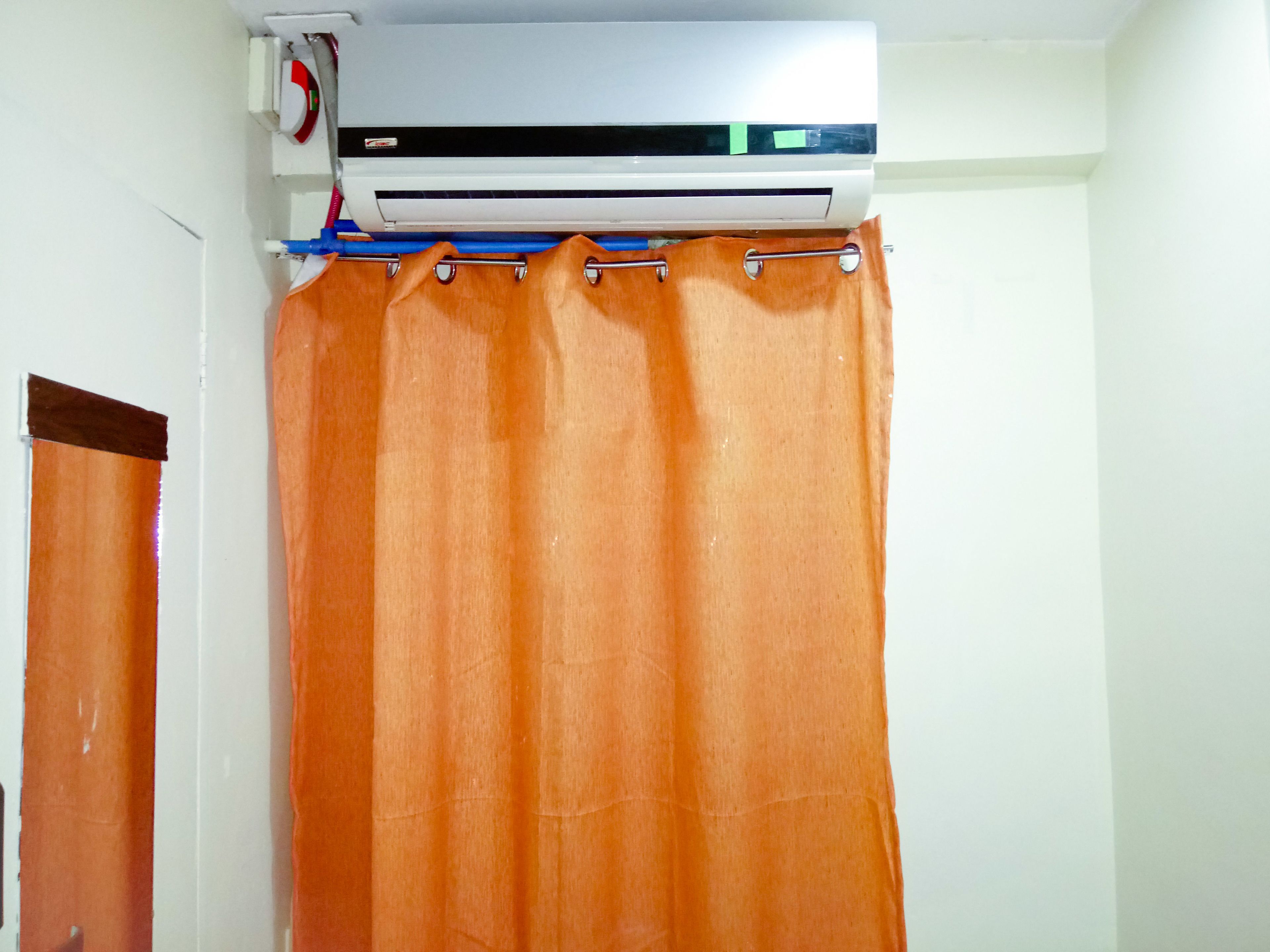 An air conditioning unit mounted above a bathroom with an orange shower curtain.