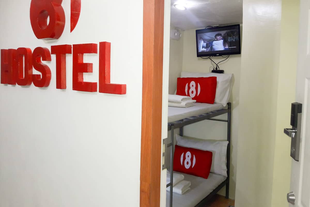 Quarto de hostel com beliches, uma TV presa na parede e um aviso com o nome do hostel.