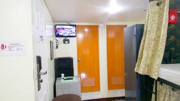 A hotel room with a bed, a television mounted on the wall, a small table, and a chair. There is a sign on the wall indicating room number 18 and a safety notice.