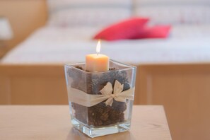 Un candelabro de cristal cuadrado con una vela encendida, piñas y una cinta blanca sobre una mesa de madera.