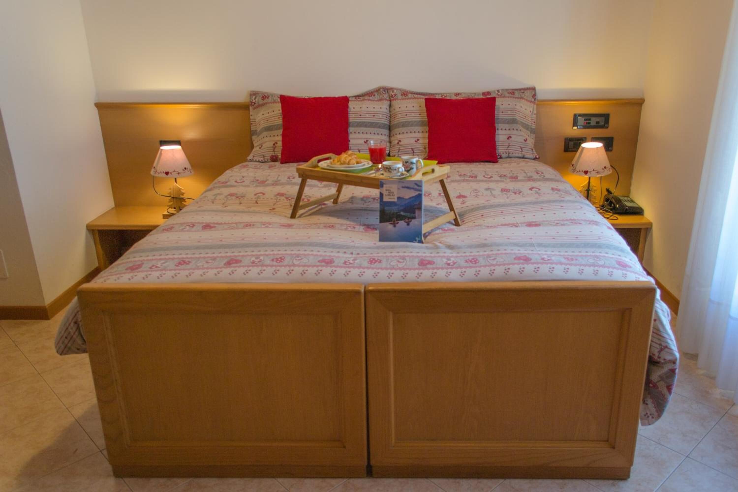 Ein Doppelbett mit Holzbettrahmen, zwei Nachttische mit Lampen und ein Tablett mit Frühstücksgebäck auf dem Bett.
