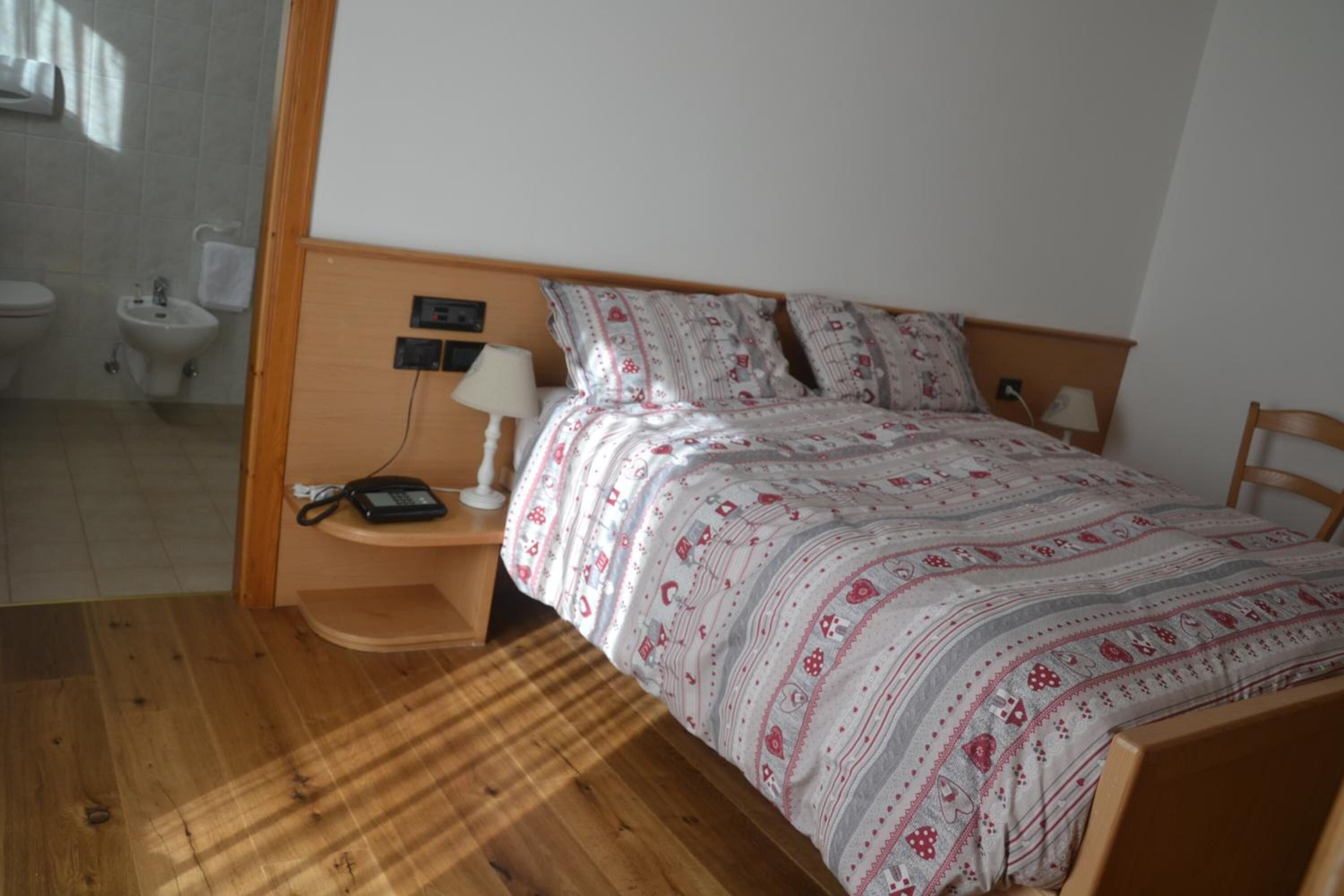 Un dormitori amb un llit de fusta, una taula de nit amb una làmpada i una petita estanteria amb un telèfon.