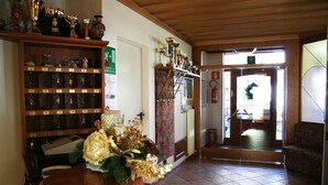 A room with a wooden ceiling, a trophy display, a floral arrangement, and a door leading to another area. - Meublè Rosalpina (Valdidentro)