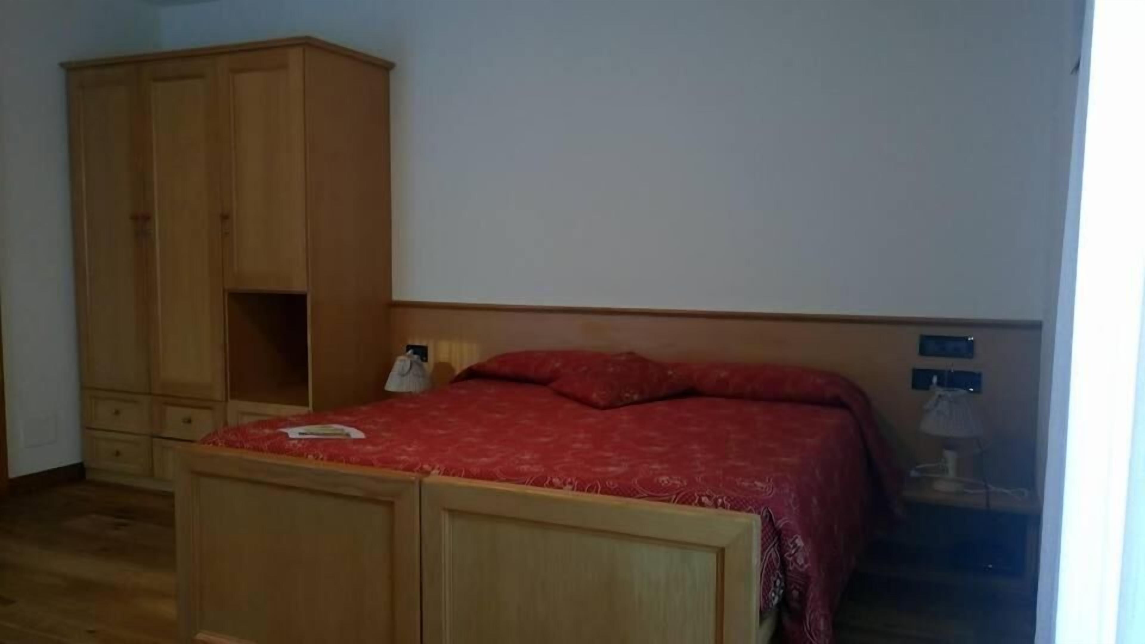 A bedroom with a wooden wardrobe, a bed with a red bedspread, and a nightstand.