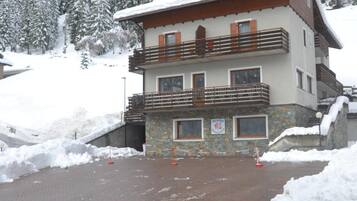 A multi-story building with a snow-covered roof and balconies, surrounded by a snowy landscape and trees.
