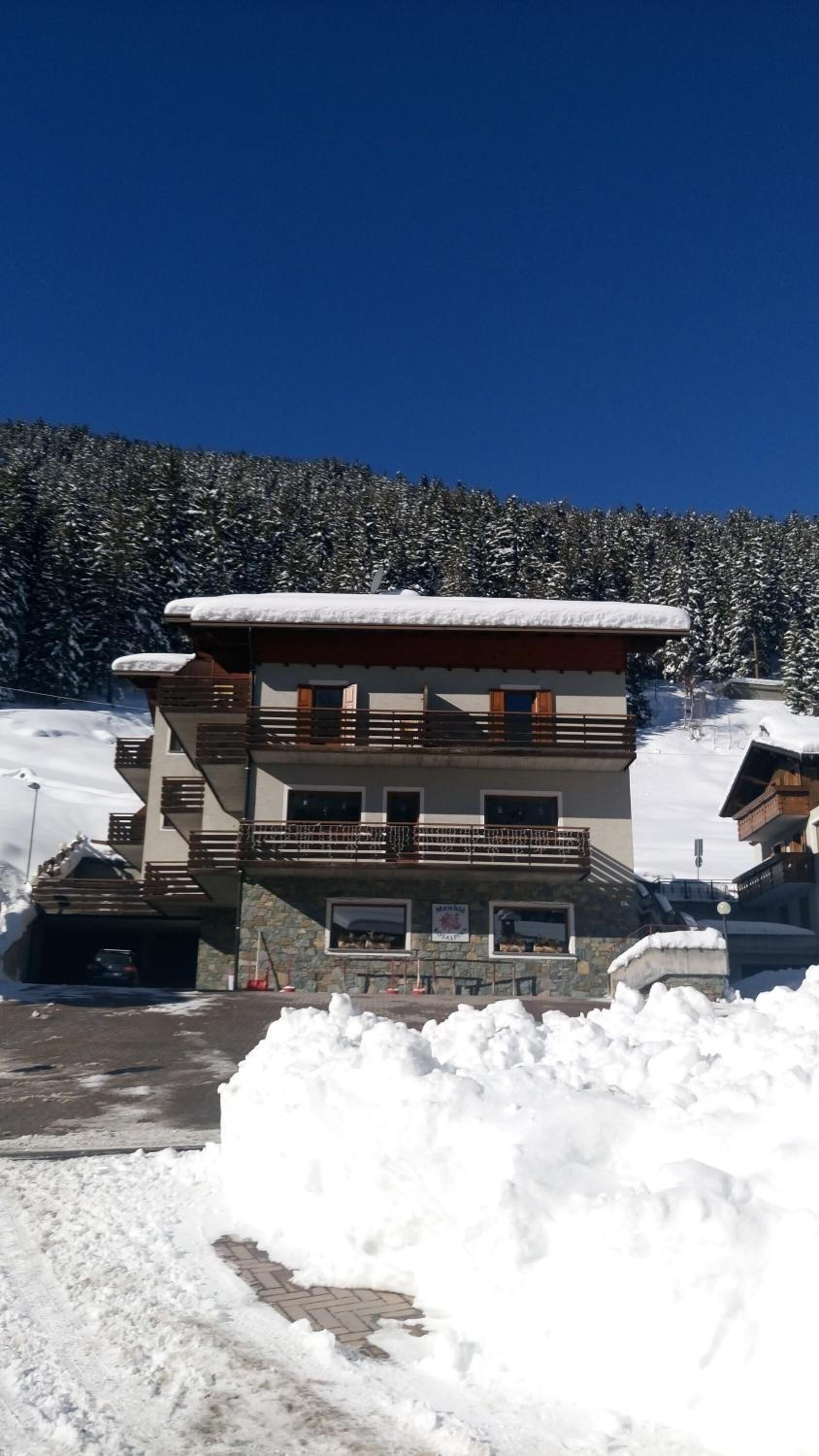 Un edificio de varios pisos con techo nevado, fachada de piedra y un balcón con barandillas.