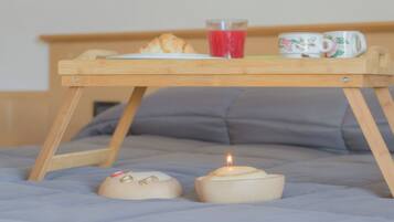 A wooden tray with a croissant, a glass of red juice, and two mugs on a bed.
