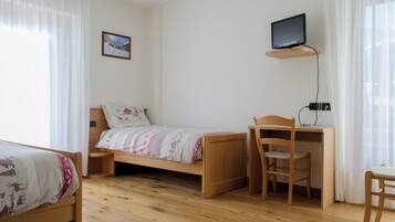 Una stanza con un letto, una scrivania con una sedia, un televisore su uno scaffale e un quadro appeso al muro.
