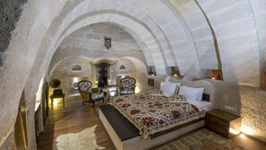 A stone-walled bedroom with a bed, two chairs, a small table, and a fireplace.