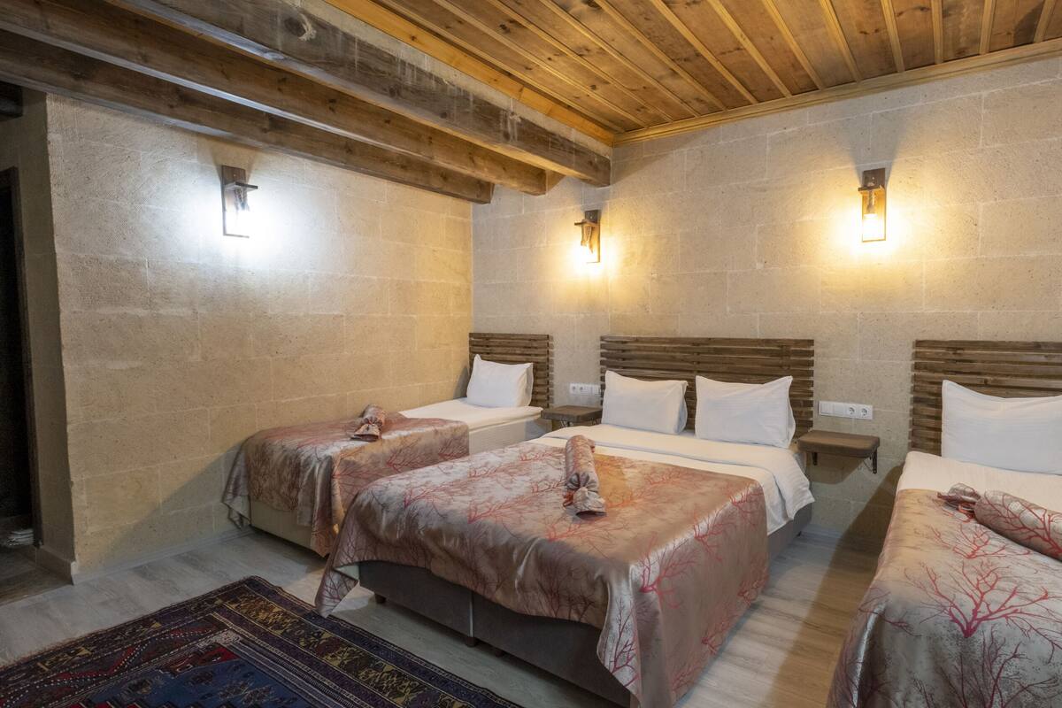Una habitación con tres camas, vigas de madera en el techo y paredes de piedra.