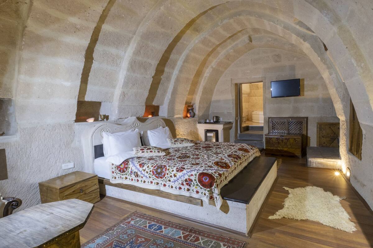 Una habitación rústica de piedra con una cama, muebles de madera y un televisor.