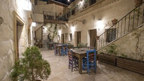 A courtyard with stone flooring, wooden tables and chairs, and a staircase with wrought iron railings.