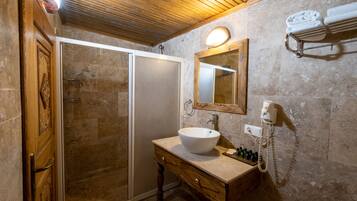 Un baño con puerta de madera, cabina de ducha con mampara de vidrio, lavamanos con espejo y toallero con toallas.