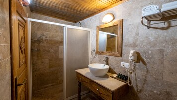 Un baño con puerta de madera, cabina de ducha con mampara de vidrio, lavamanos con espejo y toallero con toallas.