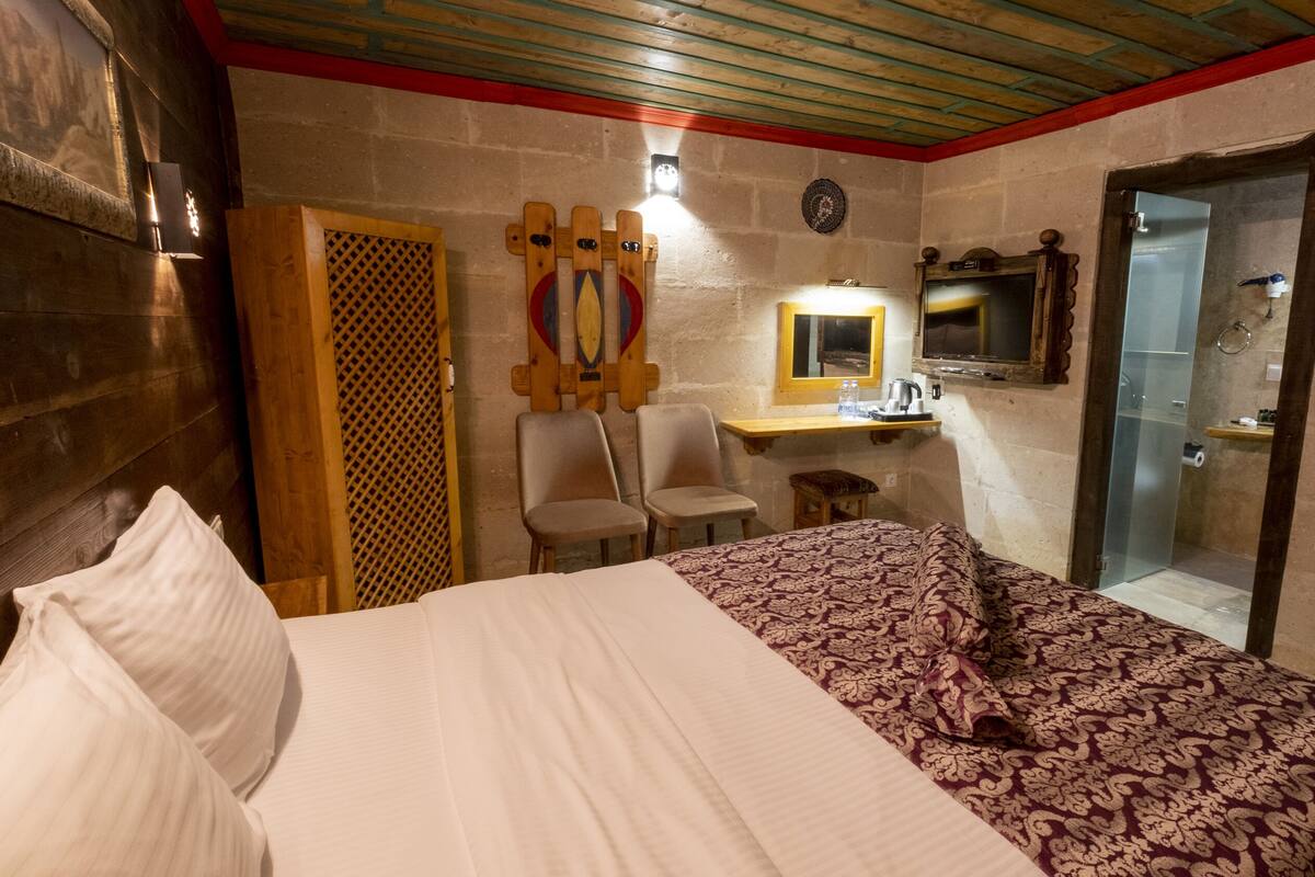 Habitación de hotel con cama, dos sillas, una mesita, un espejo y zona de ducha.
