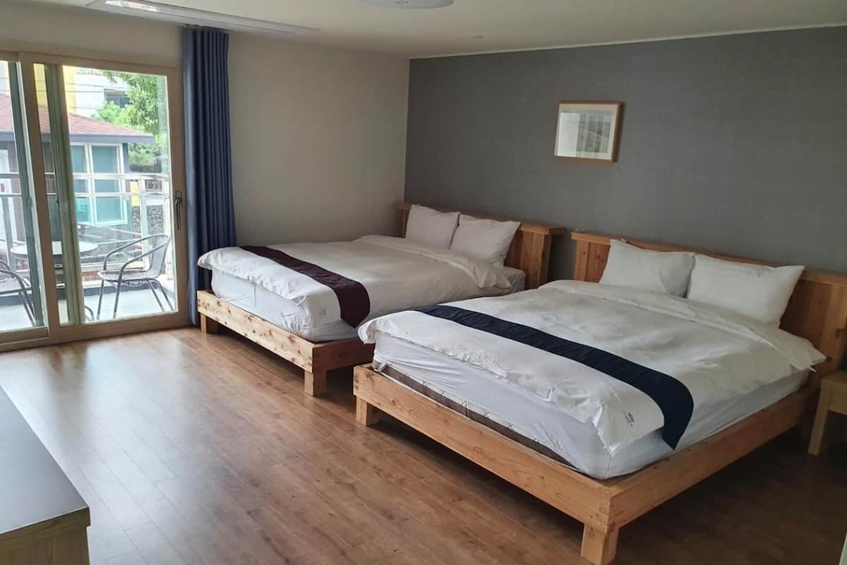 A hotel room with two wooden beds, a large window with a view of the outdoors, and a small table.