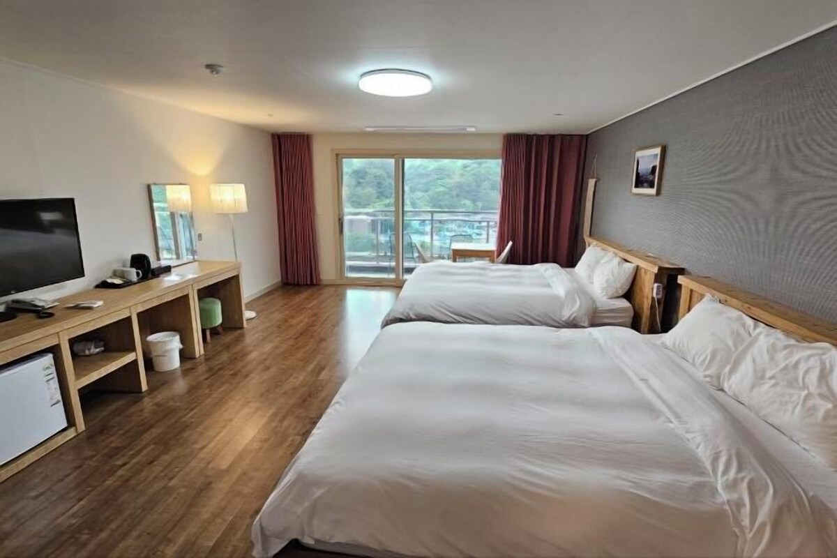 A hotel room with two beds, a TV, a desk with a lamp, and a view of the outdoors.