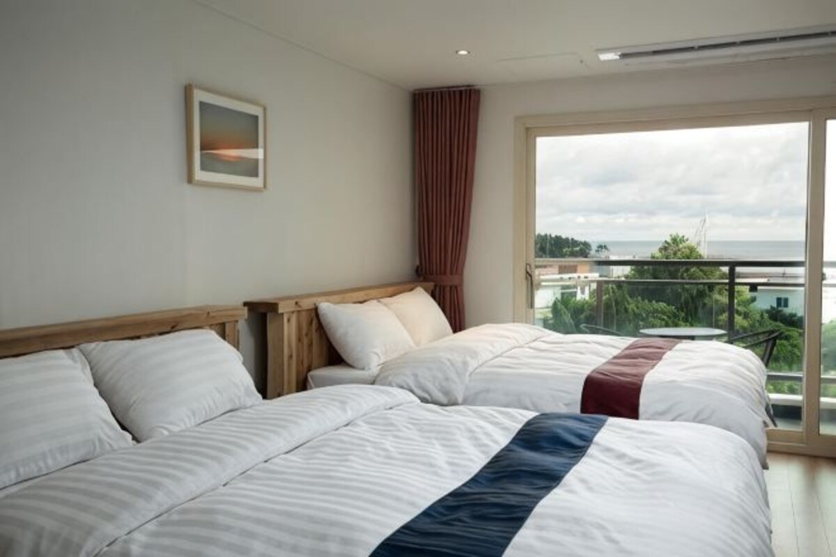 Habitación de hotel con dos camas, un ventanal grande y vistas a la ciudad.