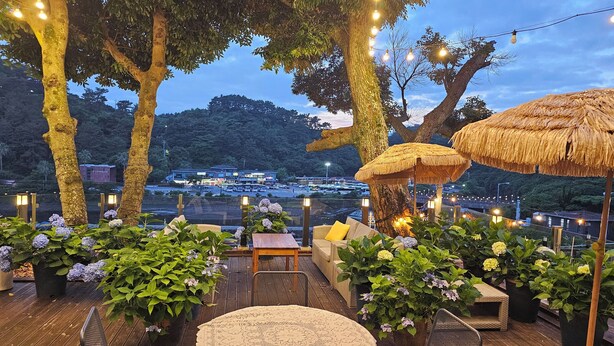An outdoor seating area with thatched umbrellas, potted plants, and string lights. - Cheonjiyeon Crystal Hotel (Seogwipo)
