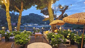 An outdoor seating area with thatched umbrellas, potted plants, and string lights. - Cheonjiyeon Crystal Hotel (Seogwipo)