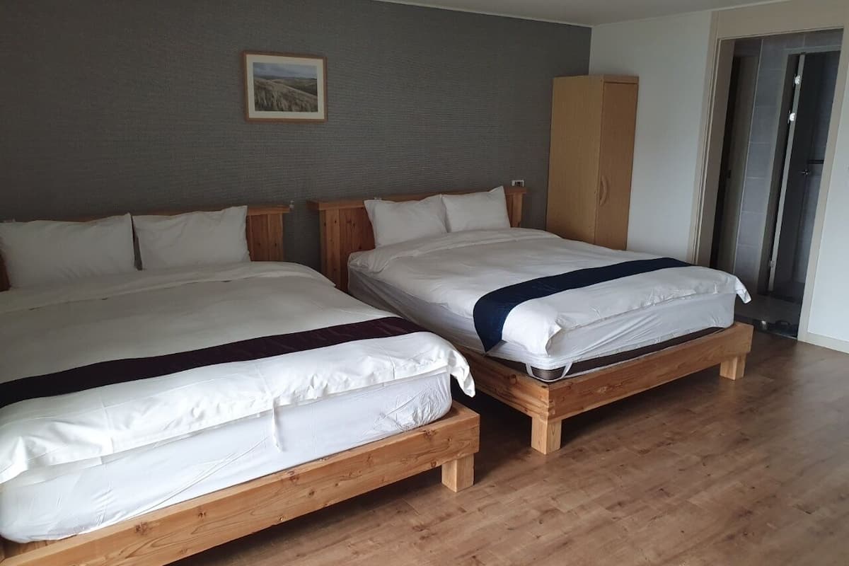 Two wooden beds with white bedding, a grey textured wall, and a wooden wardrobe.