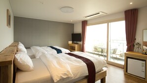 A hotel room with a bed, a TV on a stand, a small refrigerator, and a balcony with a table and chairs. - Cheonjiyeon Crystal Hotel (Seogwipo)
