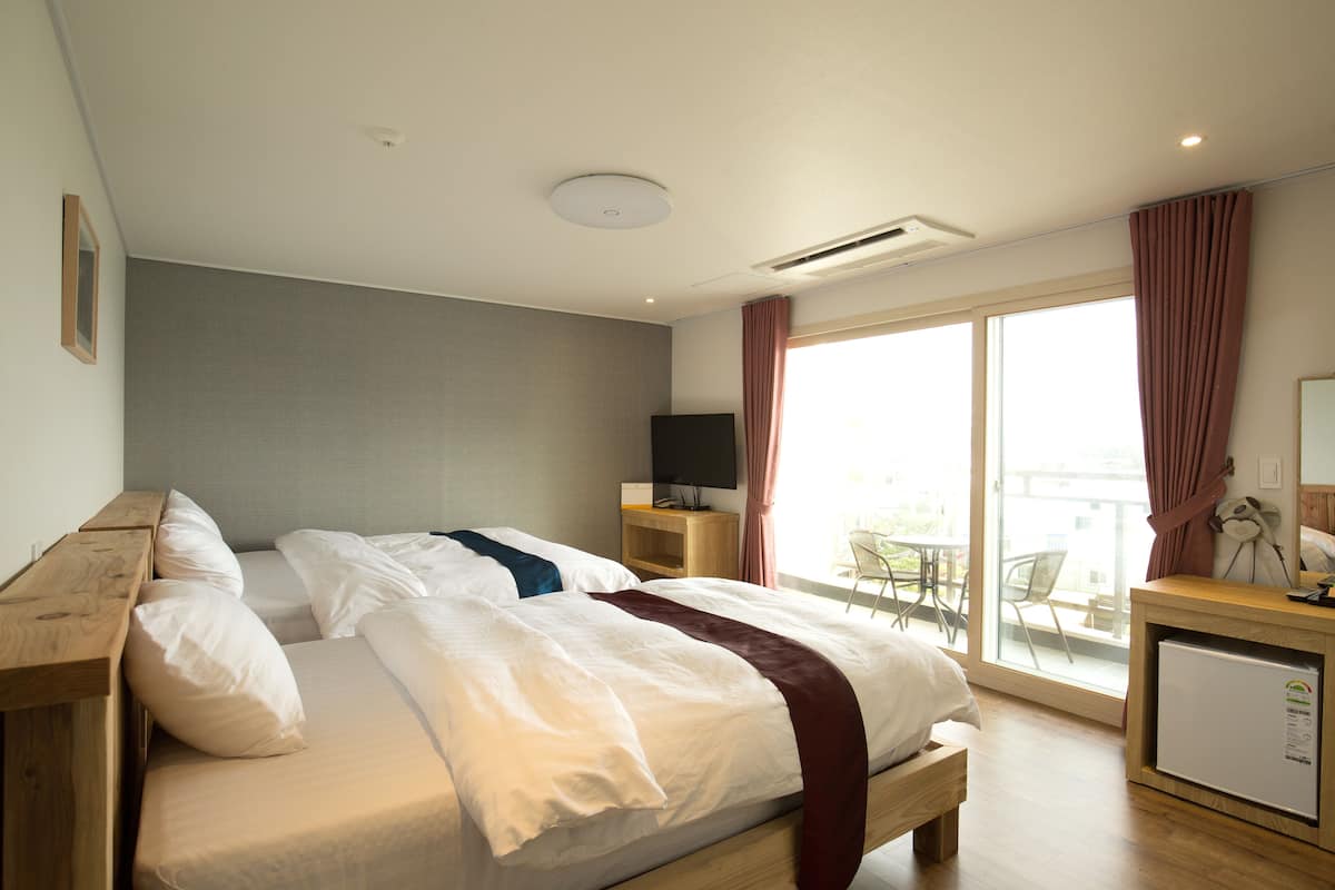 A hotel room with a bed, a TV on a stand, a small refrigerator, and a balcony with a table and chairs.