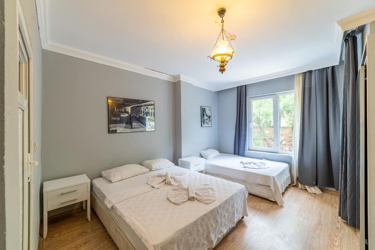 A bedroom with two beds, a nightstand, a window with curtains, and a hanging light fixture.