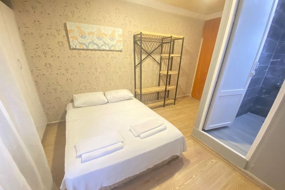 Una habitación de hotel con una cama, suelo de madera, una ventana y una pared con estampado floral.