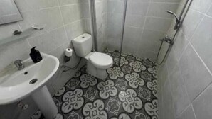 Un baño con inodoro, lavamanos y ducha. El piso tiene un diseño de baldosas con motivos.