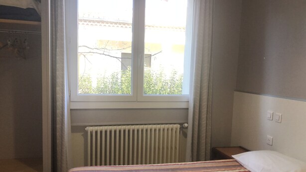 A bedroom with a bed, a window, a radiator, and a nightstand. - Hôtel les Troenes (Montpellier)