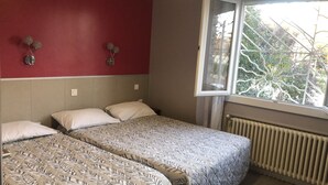 A room with two beds, a red wall, and a window with a view of trees. - Hôtel les Troenes (Montpellier)