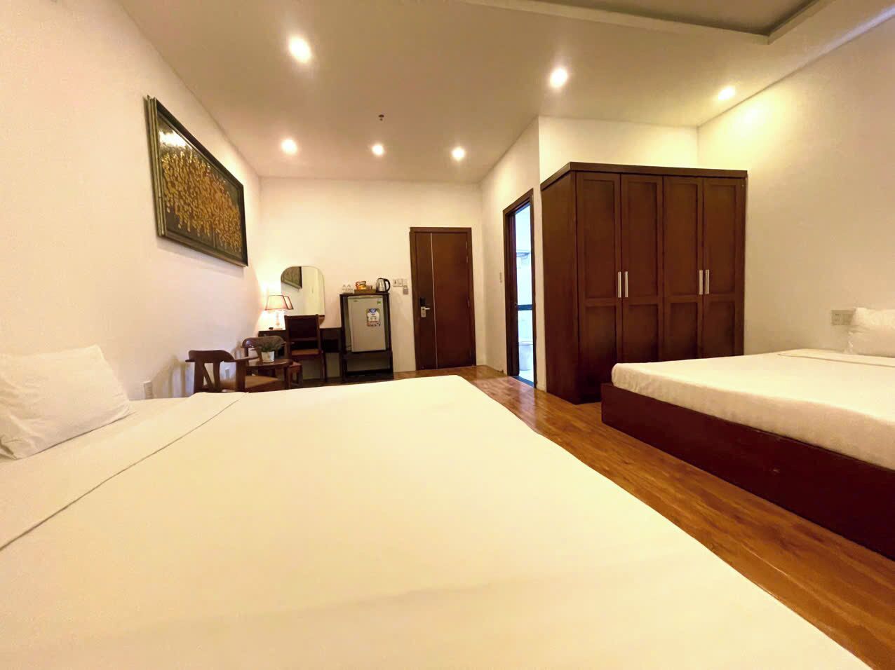 A hotel room with two beds, a desk with a chair, a small refrigerator, and a wardrobe.