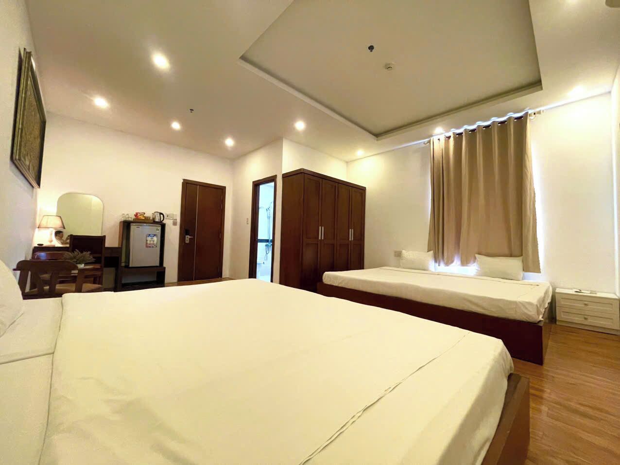A hotel room with a large bed, a desk with a lamp, a wardrobe, and a window with curtains.