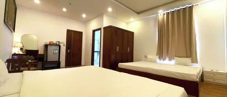 A hotel room with a large bed, a desk with a lamp, a wardrobe, and a window with curtains.