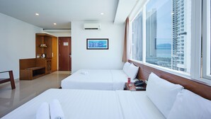 Habitación de hotel con dos camas, un escritorio, un armario y un ventanal con vista a la ciudad.