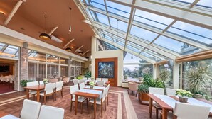 A spacious indoor area with wooden flooring, multiple tables and chairs, and large windows allowing natural light. - Hotel Ostaniec (Kroczyce)